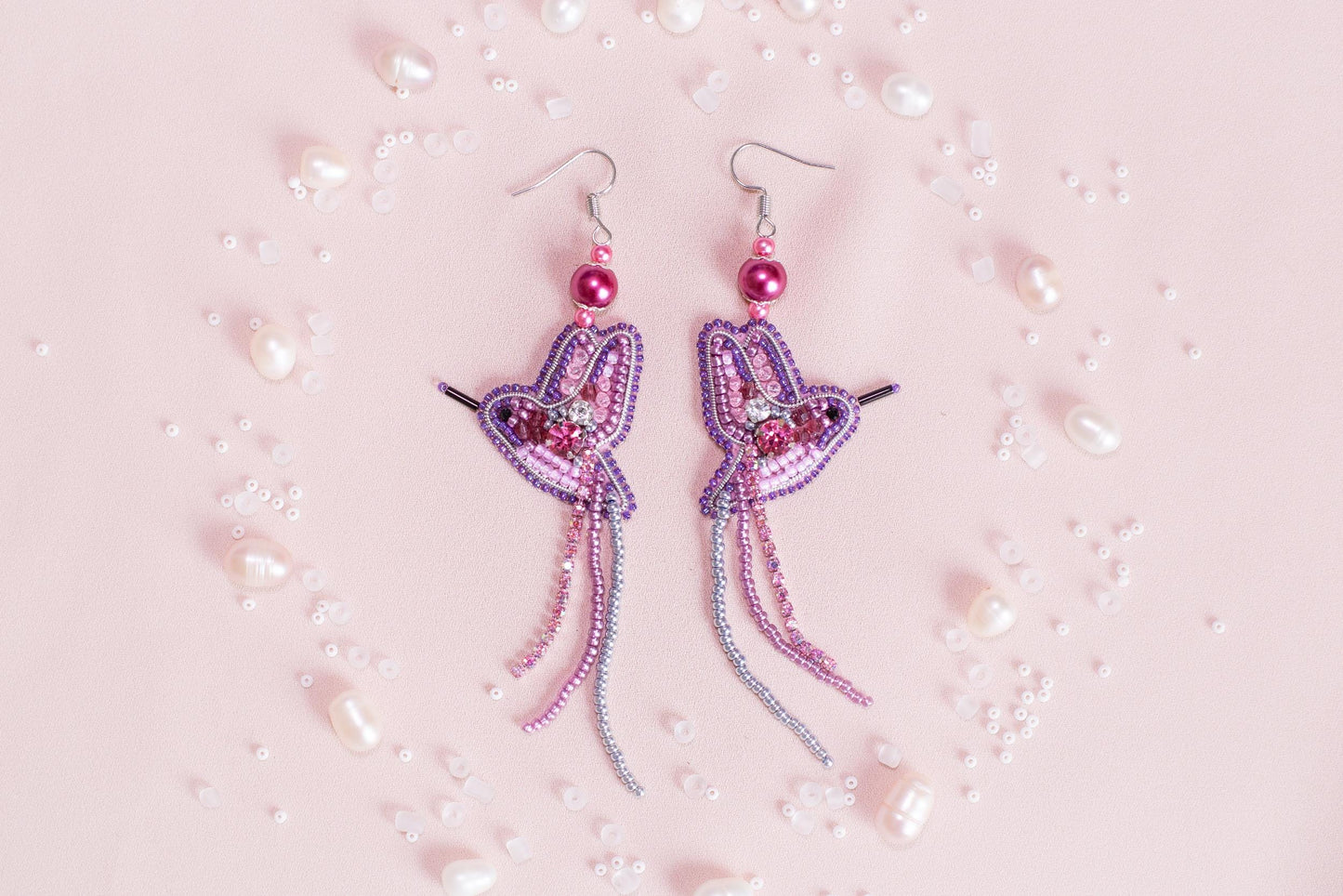 a pair of pink and purple earrings on a pink background
