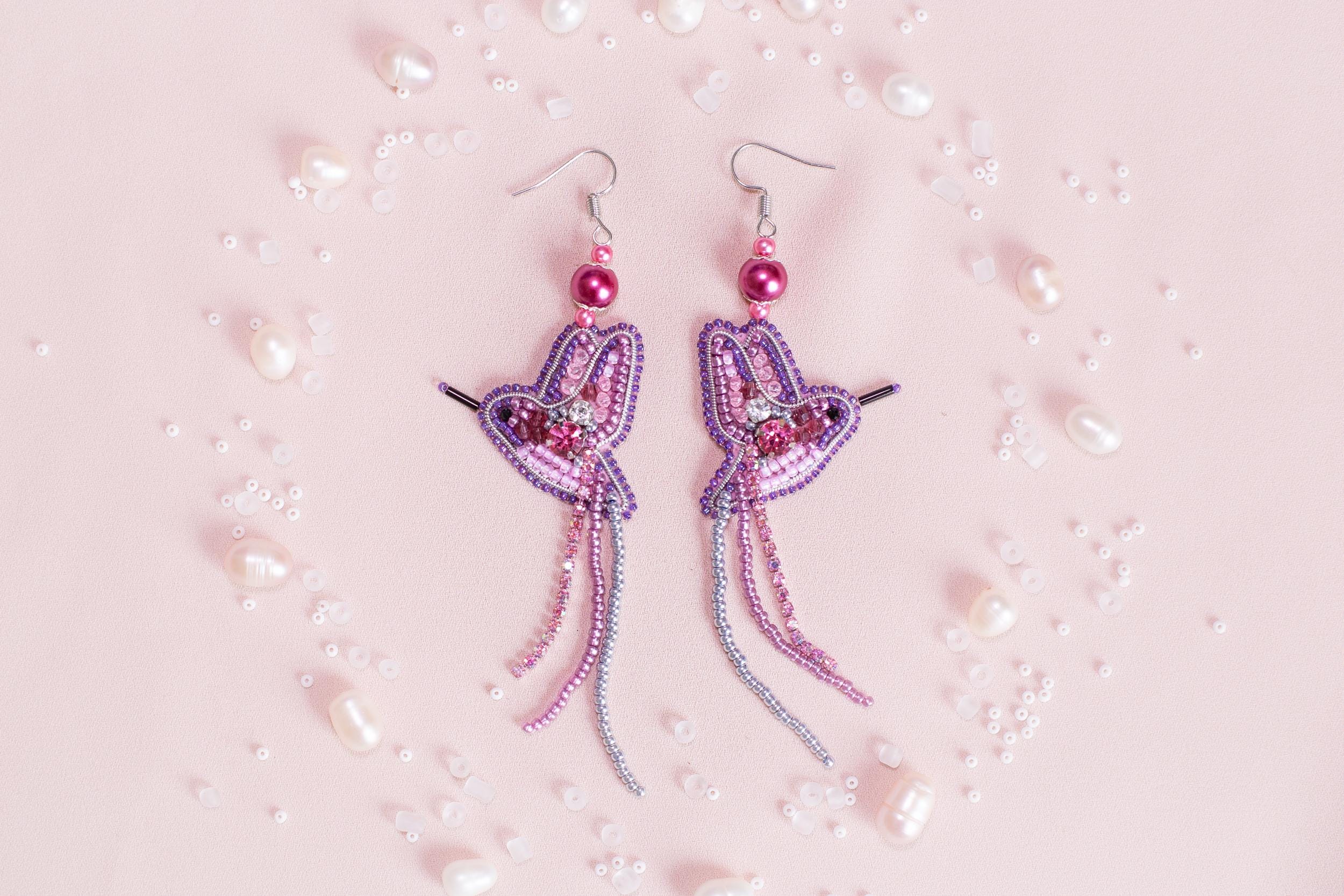 a pair of pink and purple earrings on a pink background