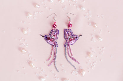 a pair of pink and purple earrings on a pink background