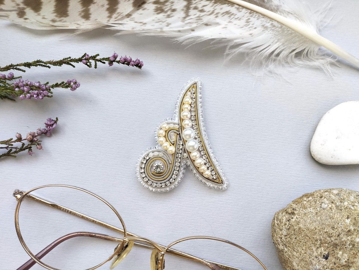 a close-up view of a decorative brooch with pearls and a gemstone, surrounded by various accessories such as glasses, feathers, and rocks.