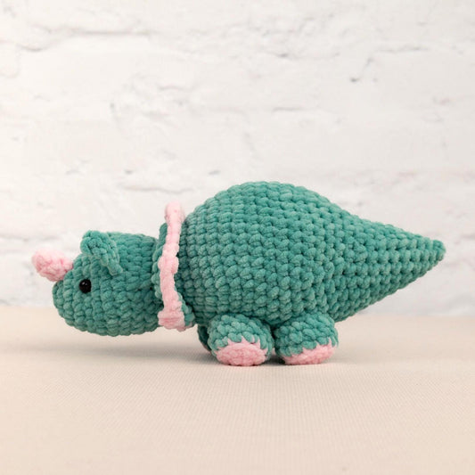 a crocheted green stuffed animal with a pink tail
