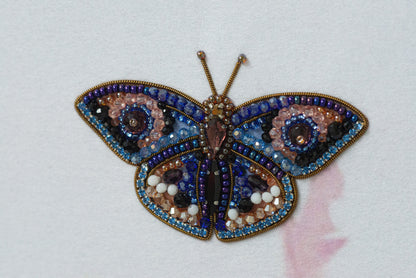 A colorful, intricately designed butterfly brooch made of various materials, including beads, stones, and sequins, is displayed against a white background.