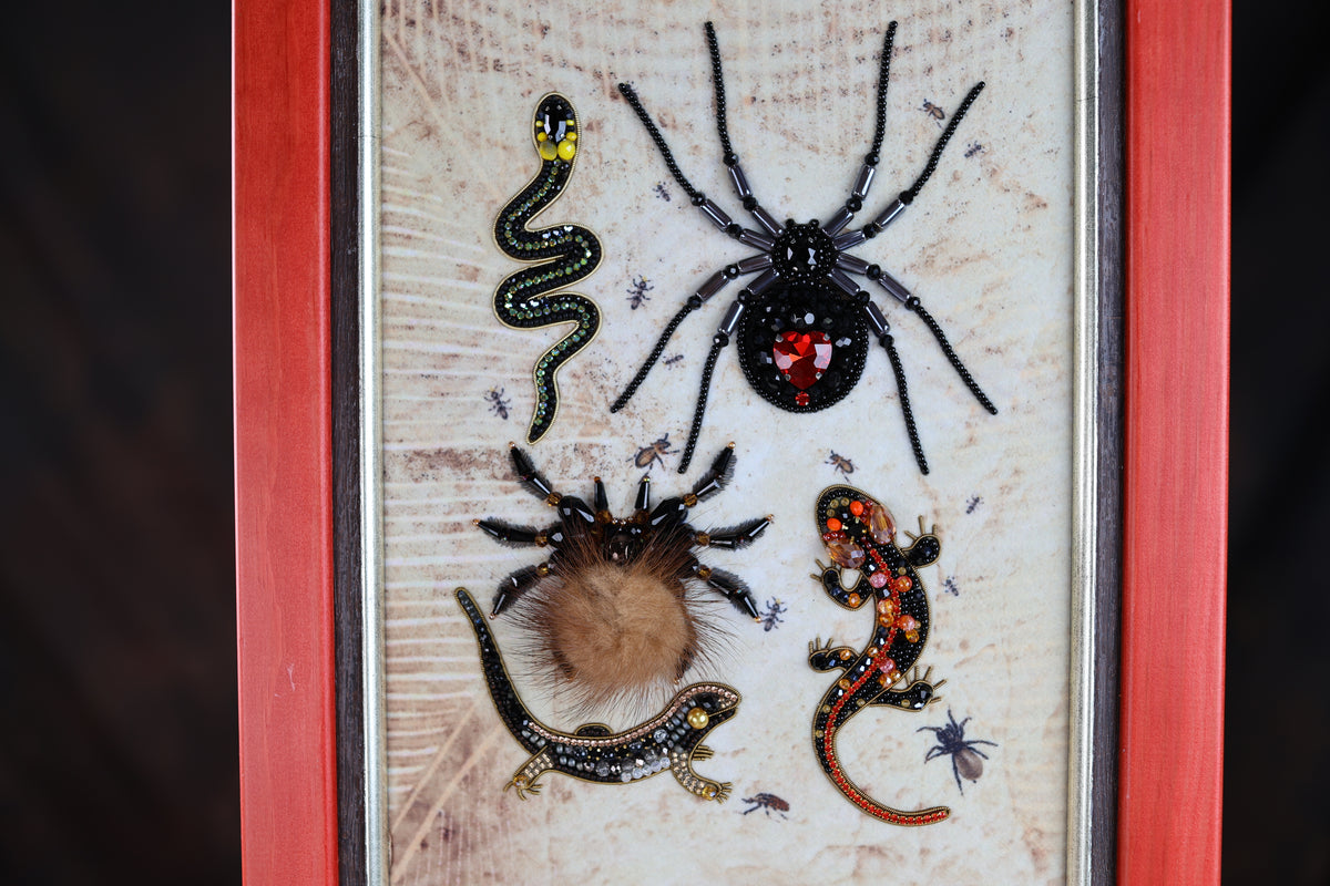 a close-up of a framed display with various insects, including a spider, a snake, a lizard, and a tarantula.