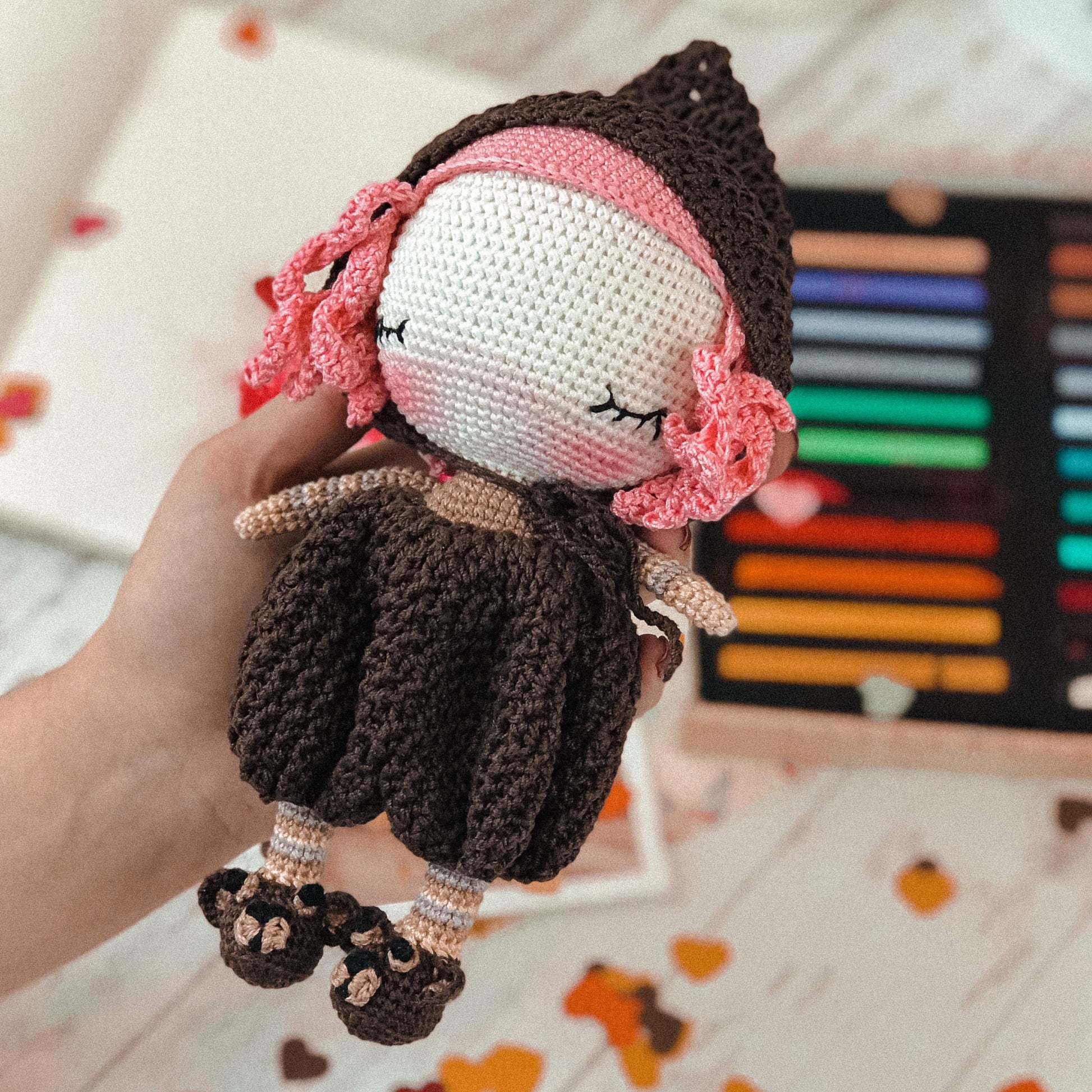 a hand holding a crocheted doll with a pink headband