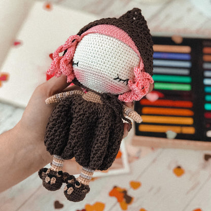 a hand holding a crocheted doll with a pink headband