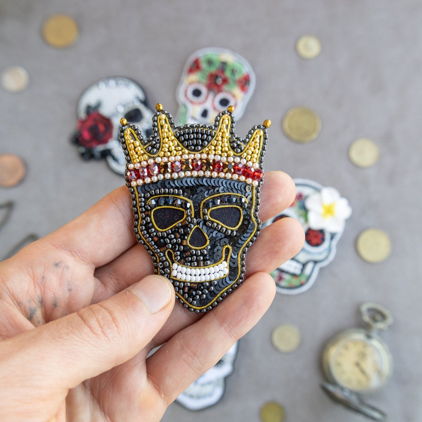 a hand holding a skull wearing a crown brooch