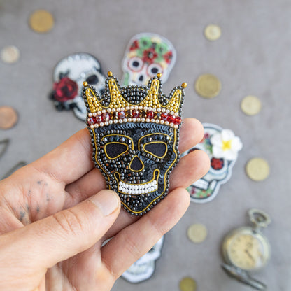 a hand holding a skull wearing a crown brooch