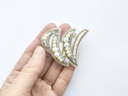 A hand holding a decorative piece of jewelry, which appears to be a bracelet or earring, against a white background.