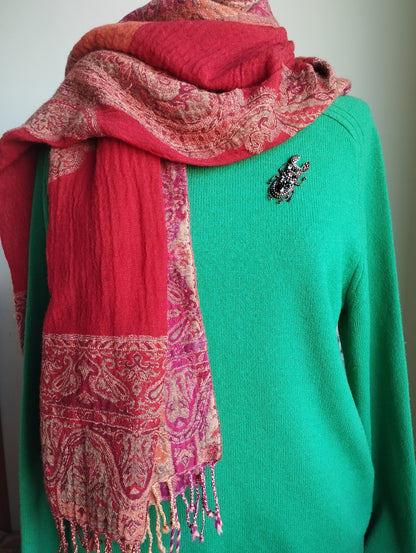 A mannequin is wearing a green sweater with a red and pink paisley-patterned scarf draped over it. The mannequin also has a brooch on its left shoulder.