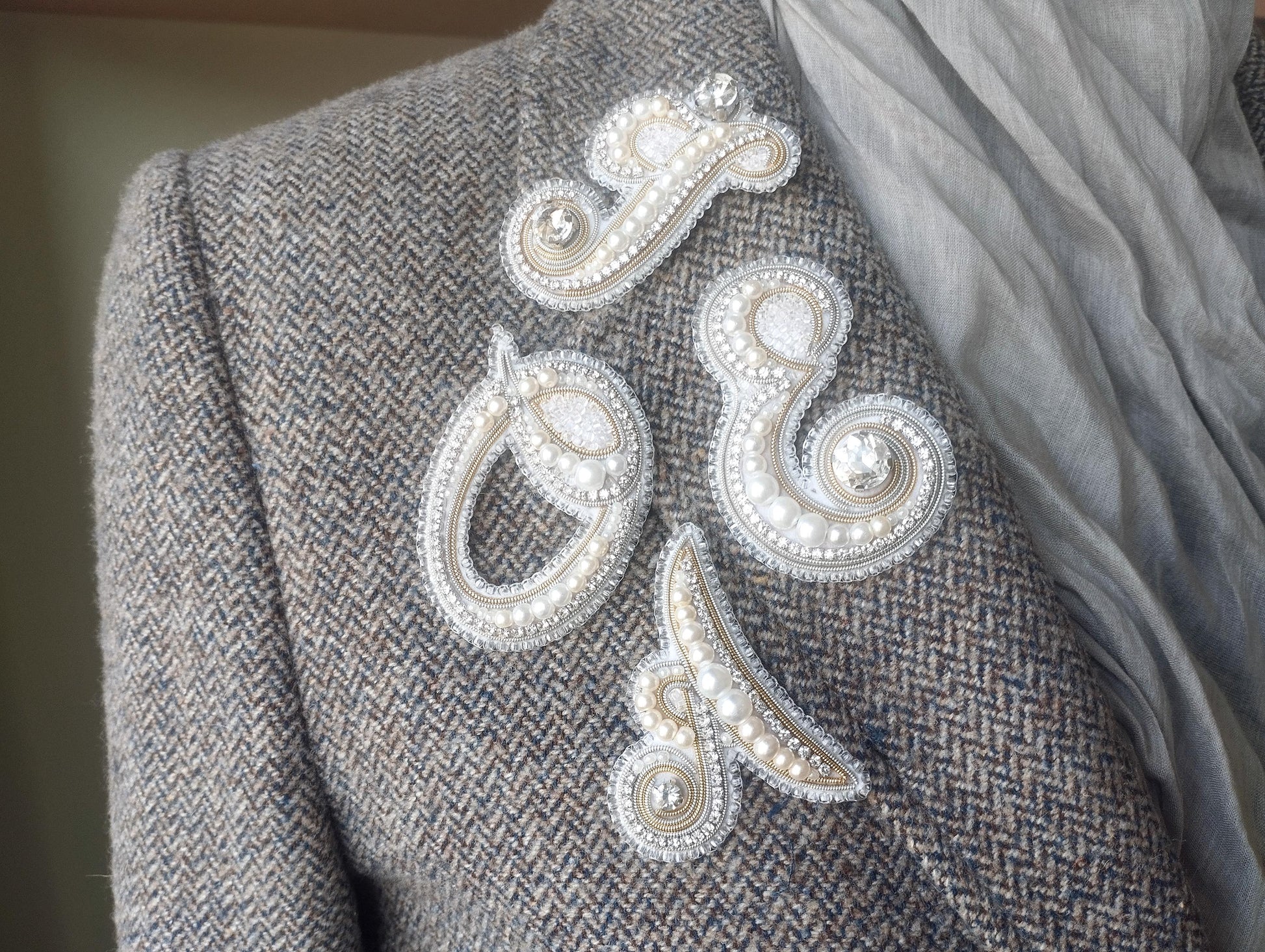 a close-up view of a person's shoulder, featuring a gray tweed jacket with decorative buttons and a scarf draped over the shoulder.