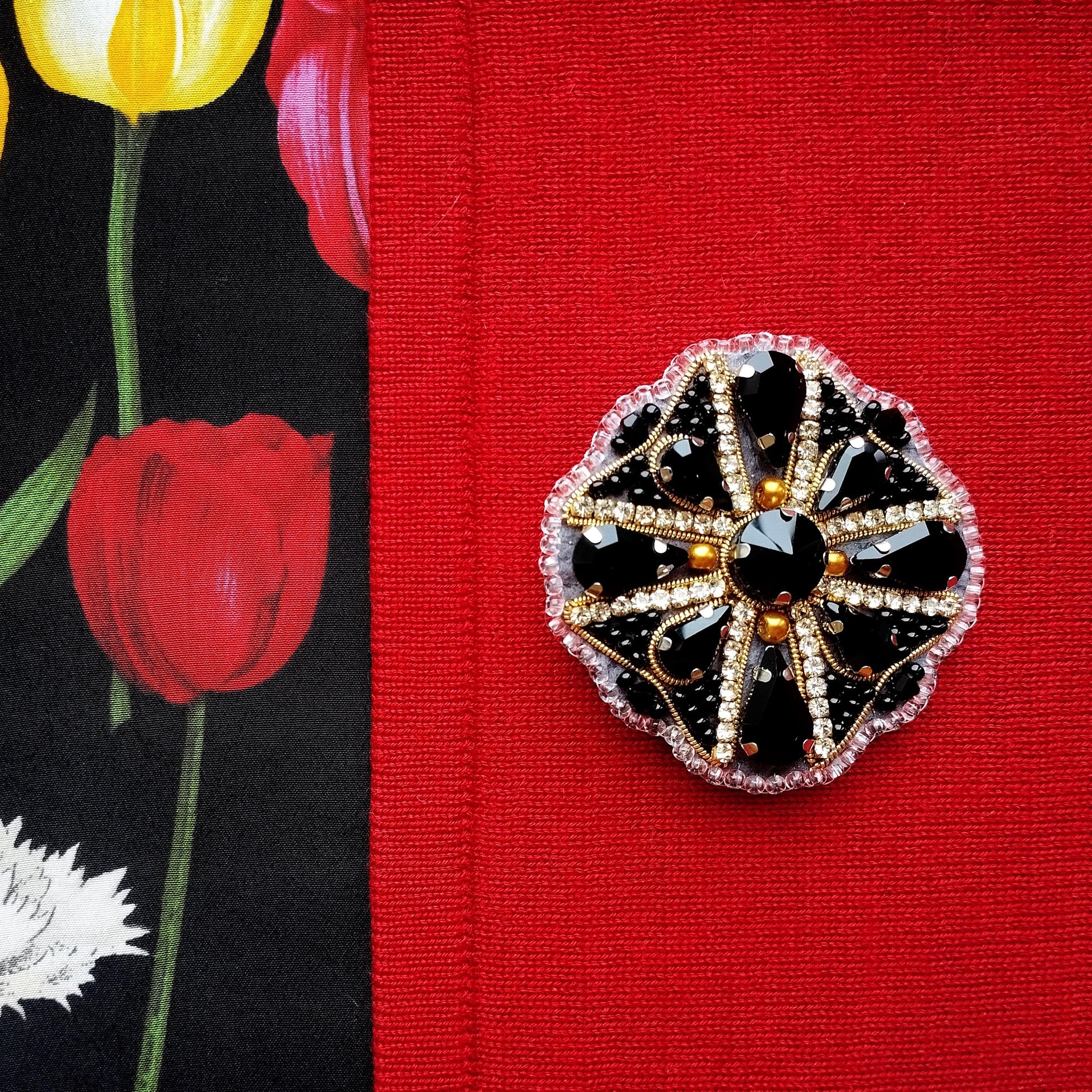 a close-up of a decorative black and gold brooch with a large central gemstone surrounded by smaller gemstones, set against a red fabric background.
