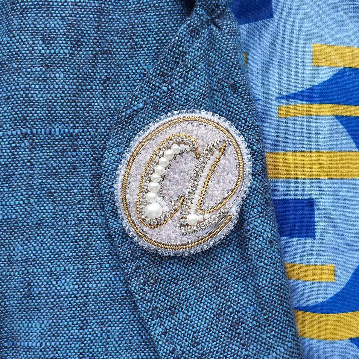 a close-up view of a blue fabric with a decorative circular emblem featuring a pearl and a letter "a" on it.