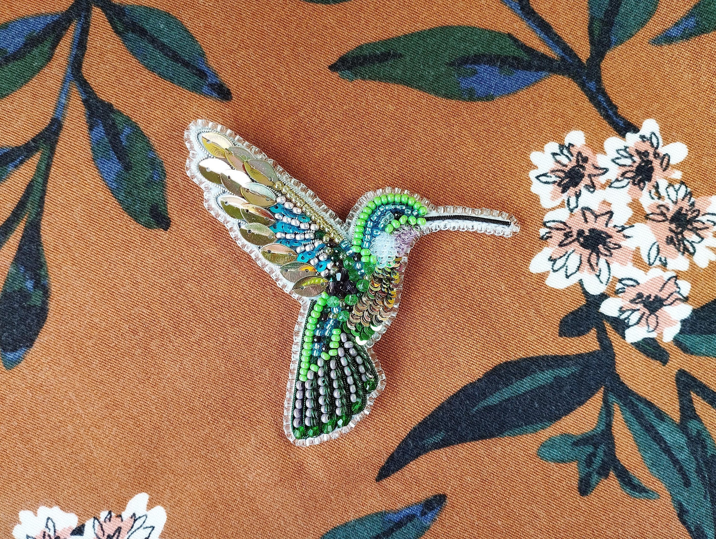 a beaded hummingbird sitting on a flowered fabric
