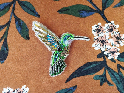 a beaded hummingbird sitting on a flowered fabric