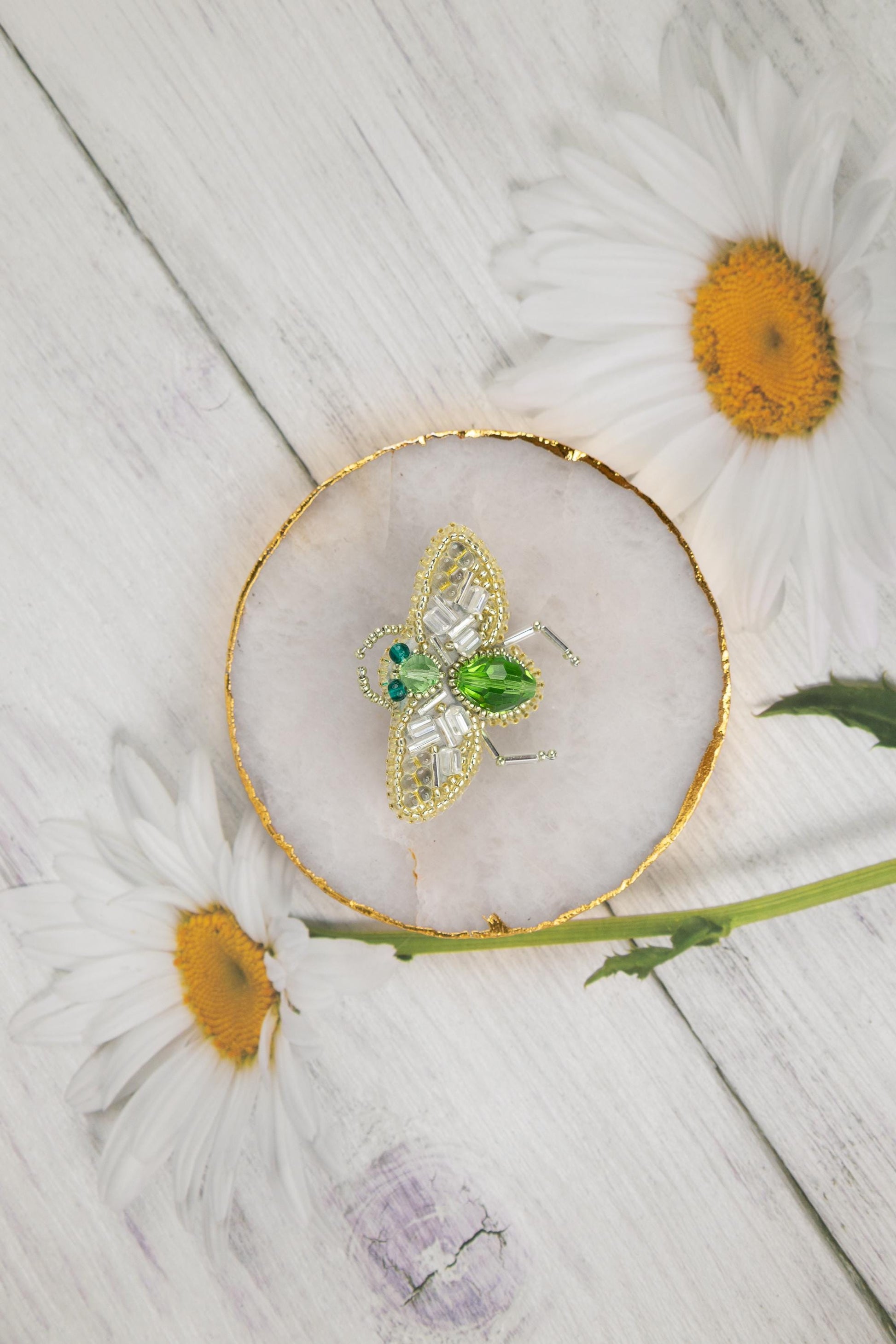 daisies and a brooch sitting on a white wooden surface