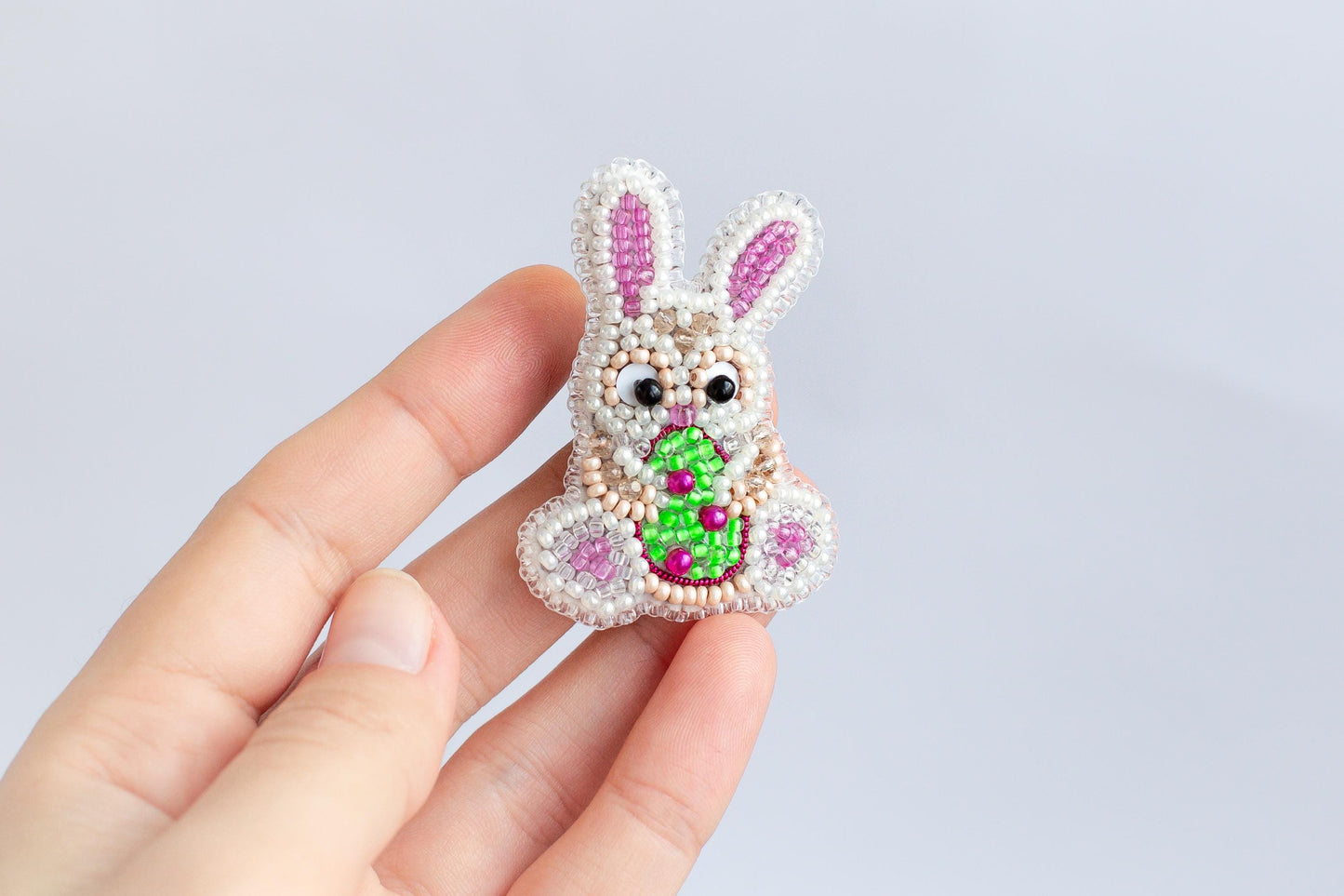 A hand holding a small, intricately beaded Easter bunny pin.