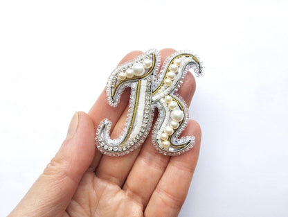 A hand holding a decorative letter 'K' made of beads, pearls, and rhinestones.