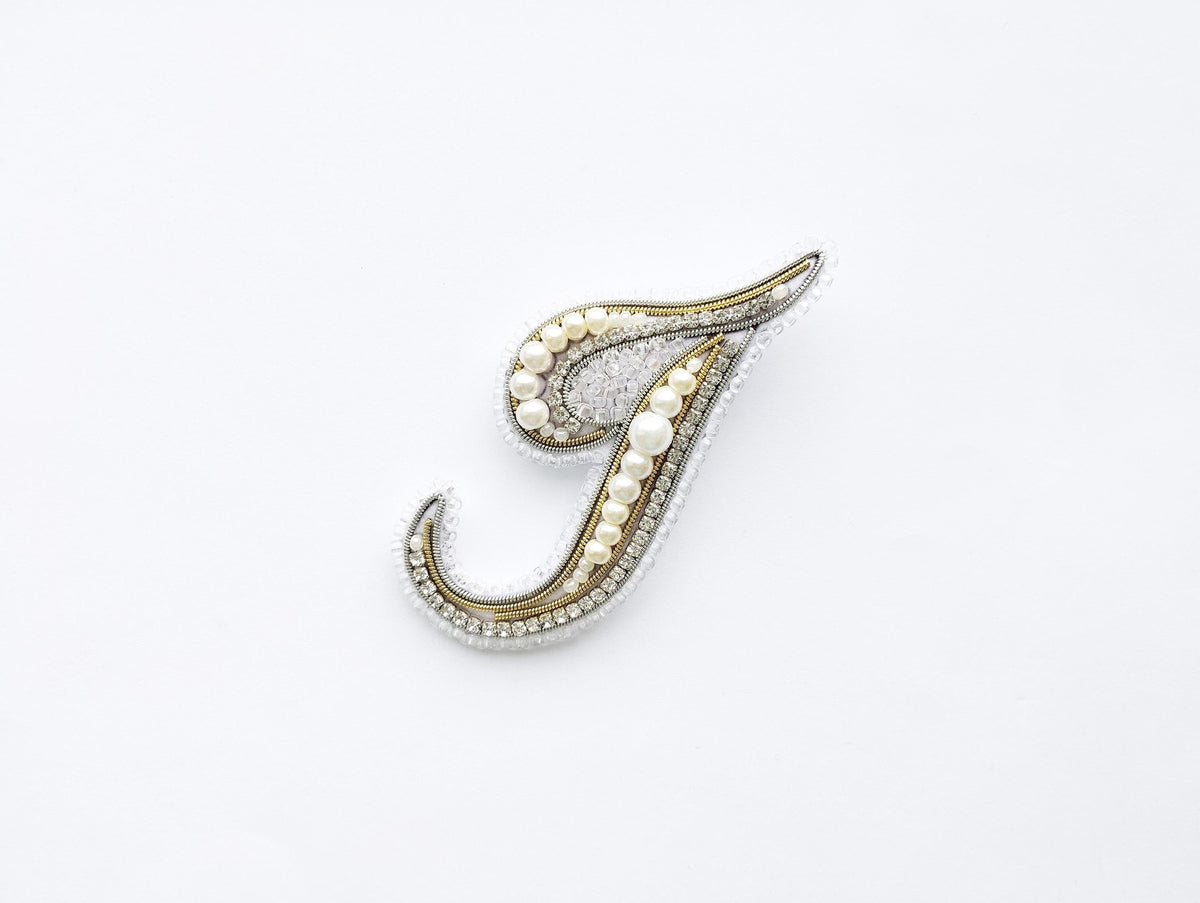 A decorative letter 'J' made of various materials, including pearls and diamonds, against a white background.