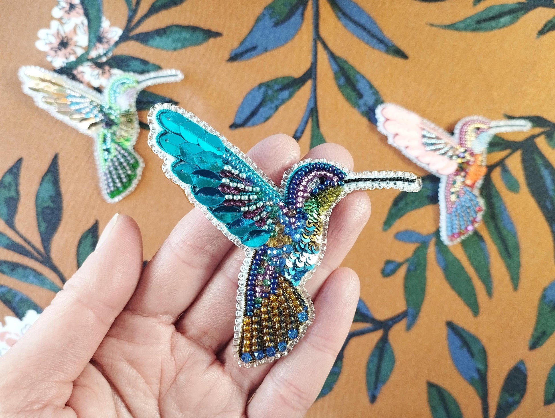 a hand is holding a beaded humming bird