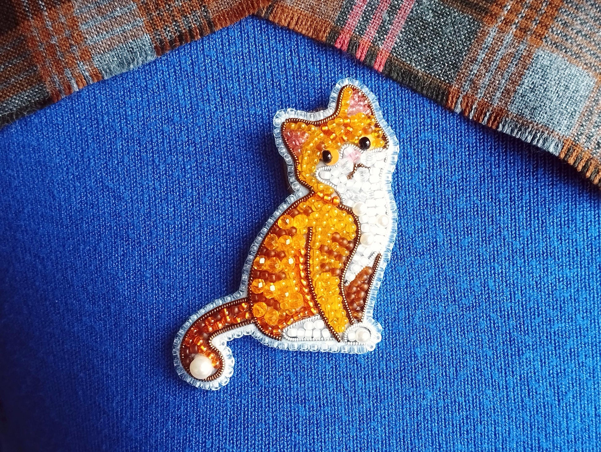 A close-up image of a cat embroidered on a blue fabric, with a plaid fabric visible in the background.