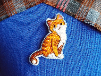 A close-up image of a cat embroidered on a blue fabric, with a plaid fabric visible in the background.