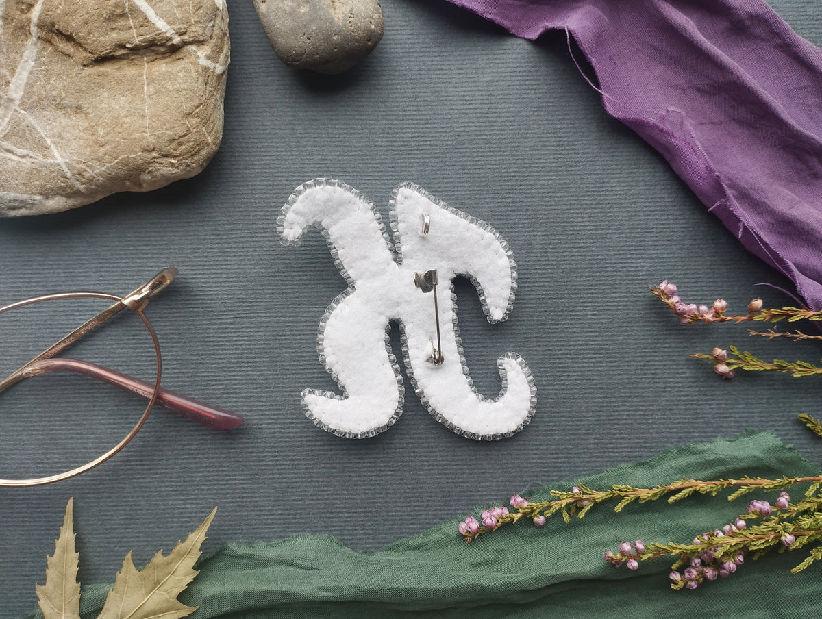 a close-up view of a white fabric piece with a pin hole design, surrounded by various objects such as a rock, a pair of glasses, and some flowers.