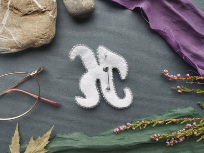 a close-up view of a white fabric piece with a pin hole design, surrounded by various objects such as a rock, a pair of glasses, and some flowers.