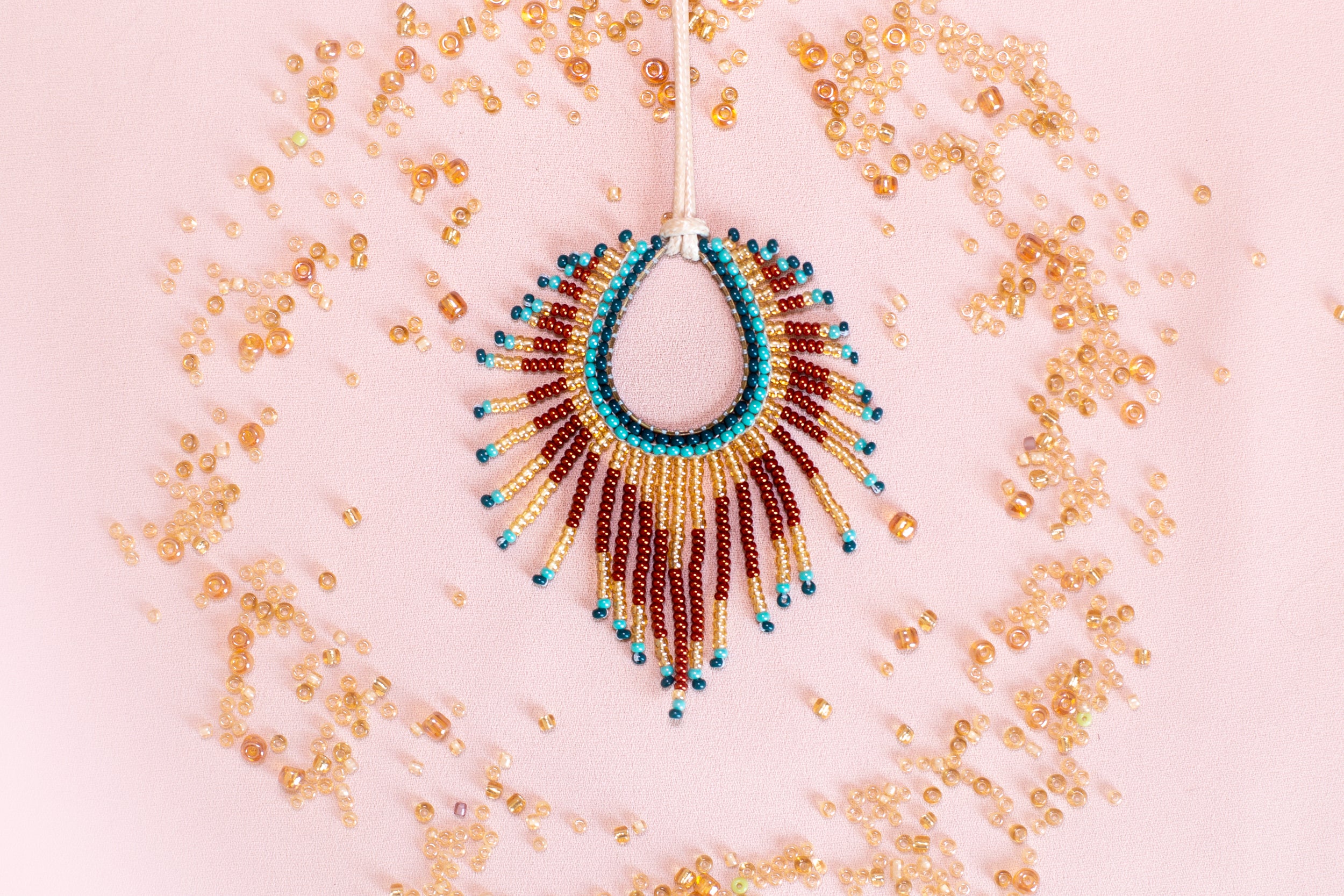 a beaded necklace with a large, colorful pendant, surrounded by scattered beads in various shades of gold, red, and blue.