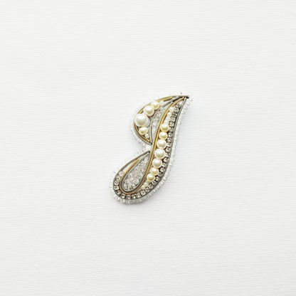 A decorative letter 'J' made of various materials, including pearls and crystals, is displayed against a white background.