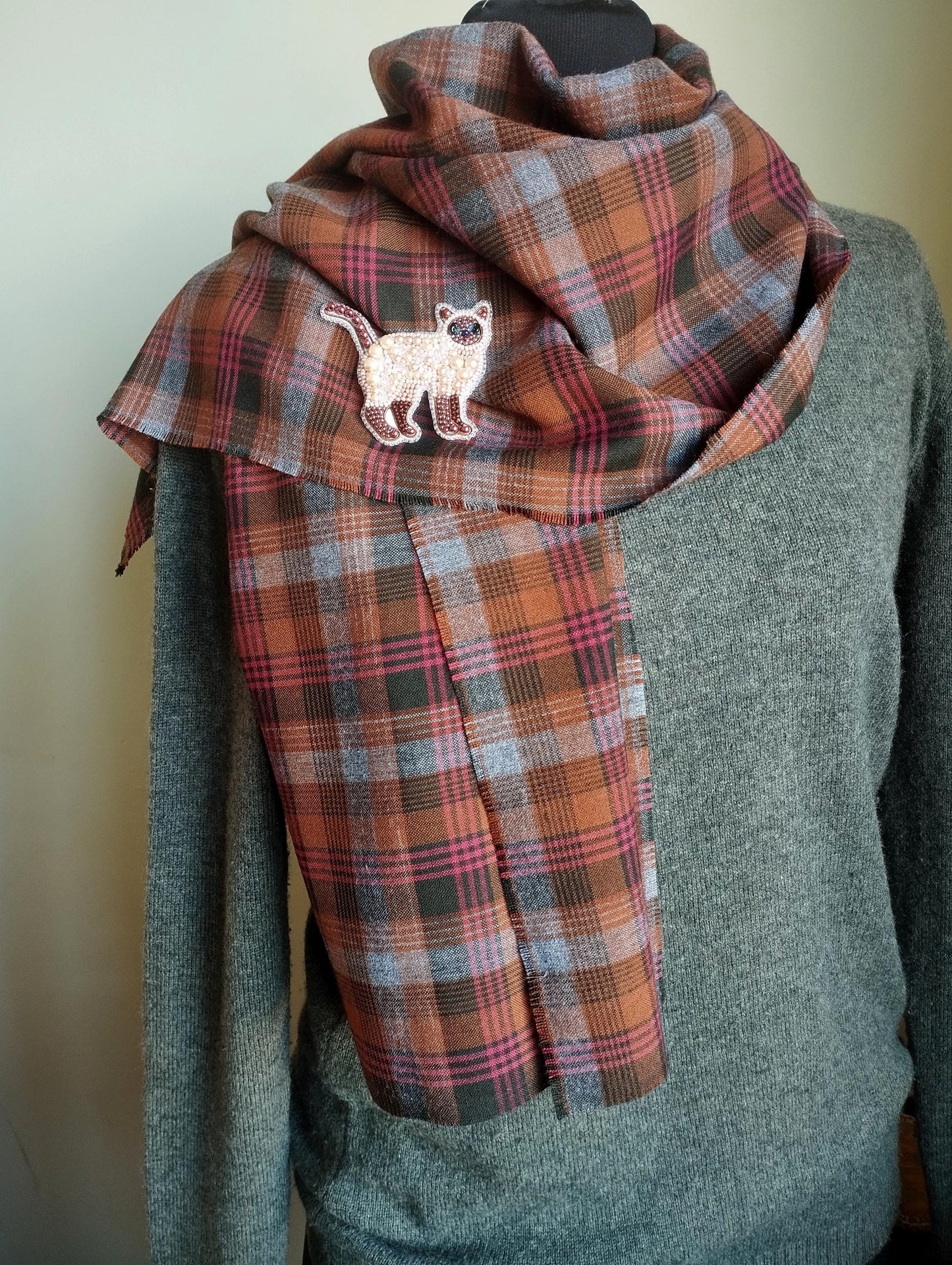 A mannequin wearing a gray sweater and a plaid scarf with a cat embroidered on it.