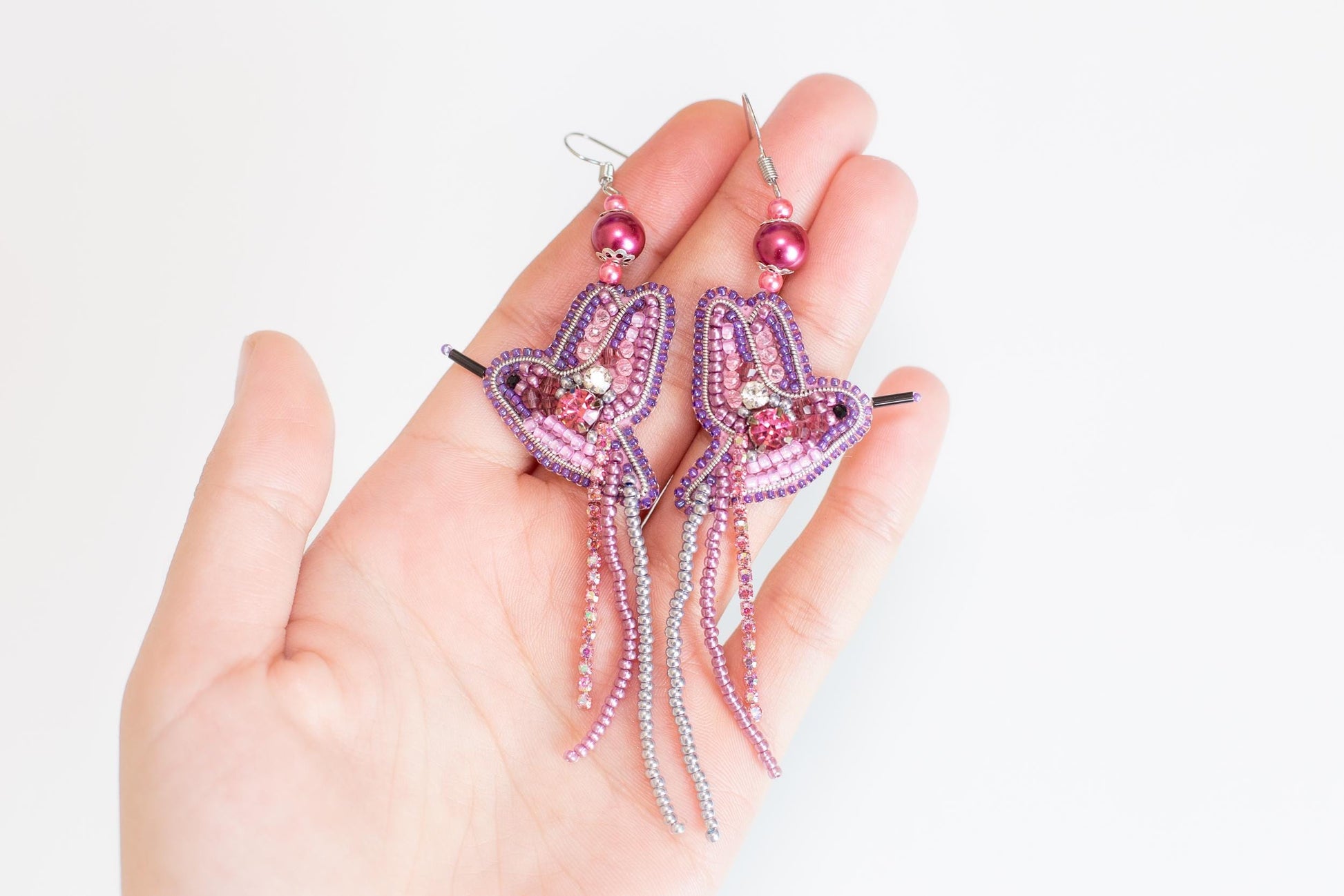a hand holding a pair of pink and purple earrings