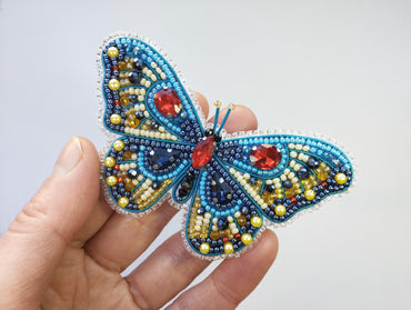 a hand holding a beaded butterfly brooch