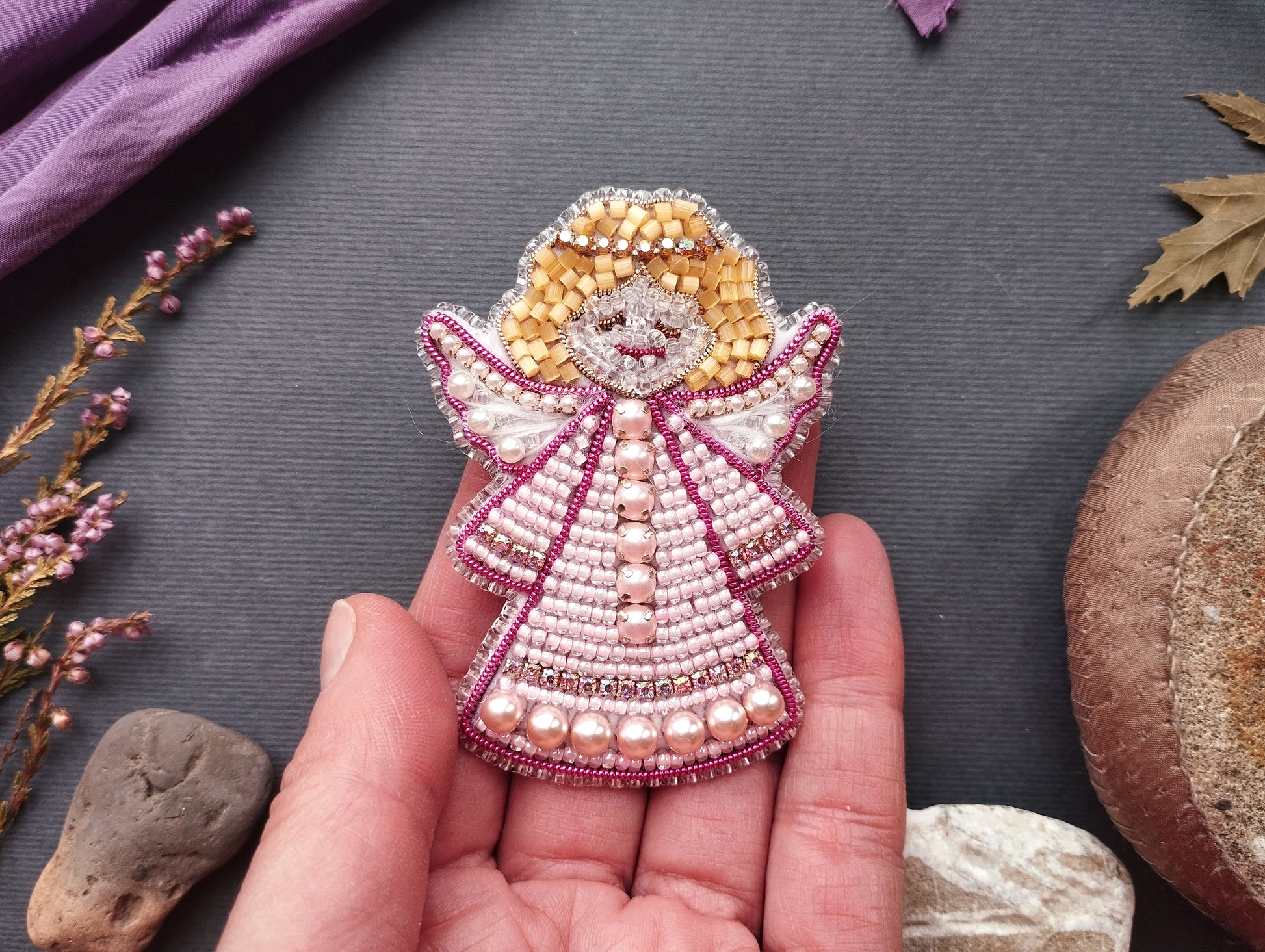 A hand holding a small, intricately beaded angel pin against a dark background.
