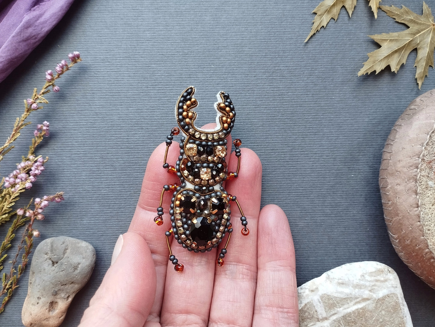 A hand holding a decorative insect brooch with intricate beading and beadwork.