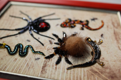 a close-up view of various insects and animals, including a spider, a lizard, and a tarantula, all intricately crafted and adorned with colorful beads and materials.
