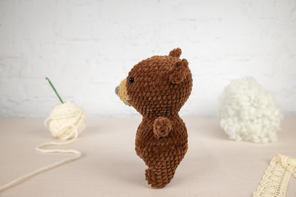 a brown teddy bear standing next to a ball of yarn