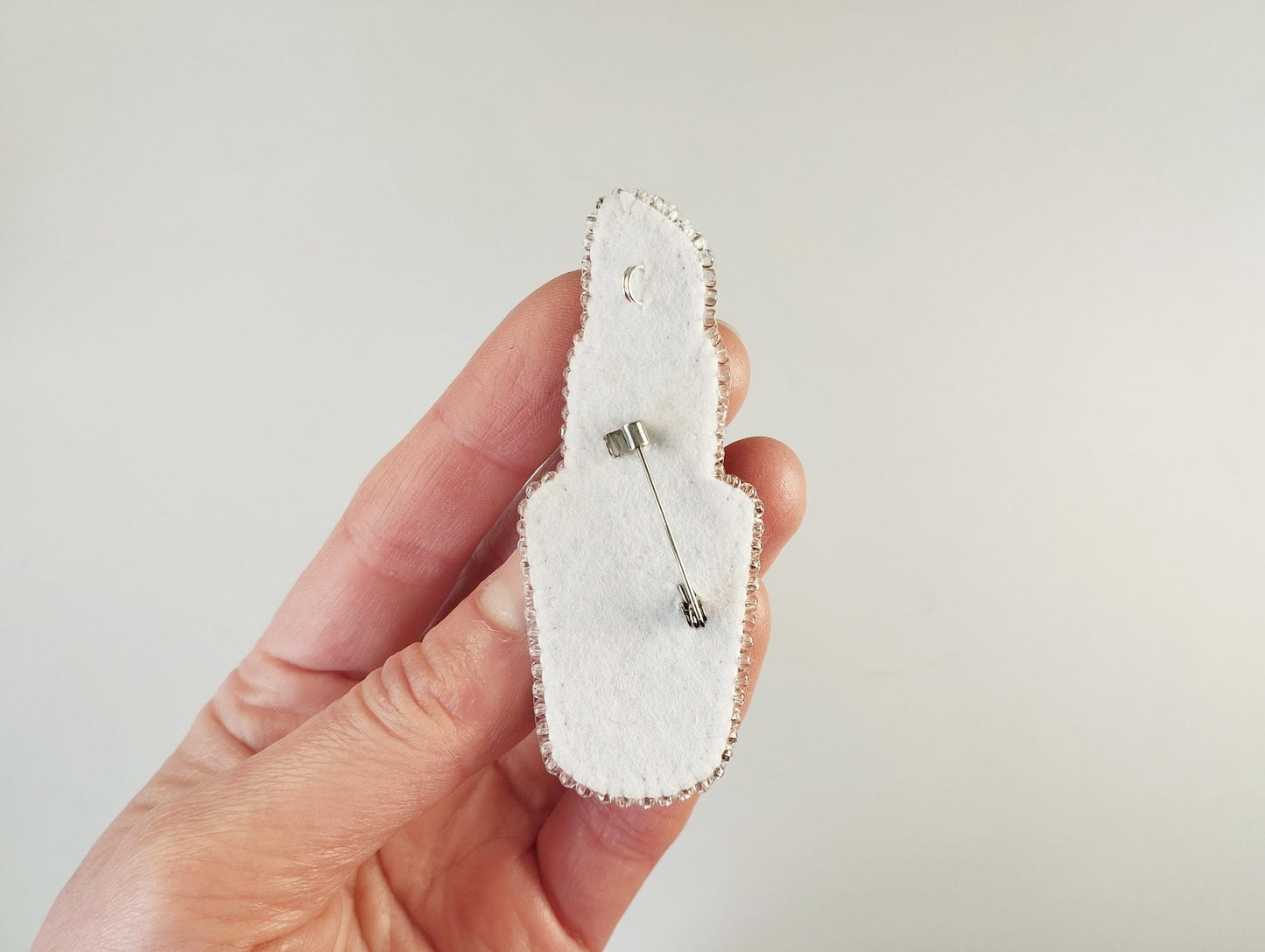 A hand holding a white pin cushion-shaped object with a pin attached to it.