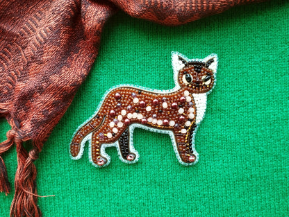 a brown and white cat-shaped embroidered piece on a green background.