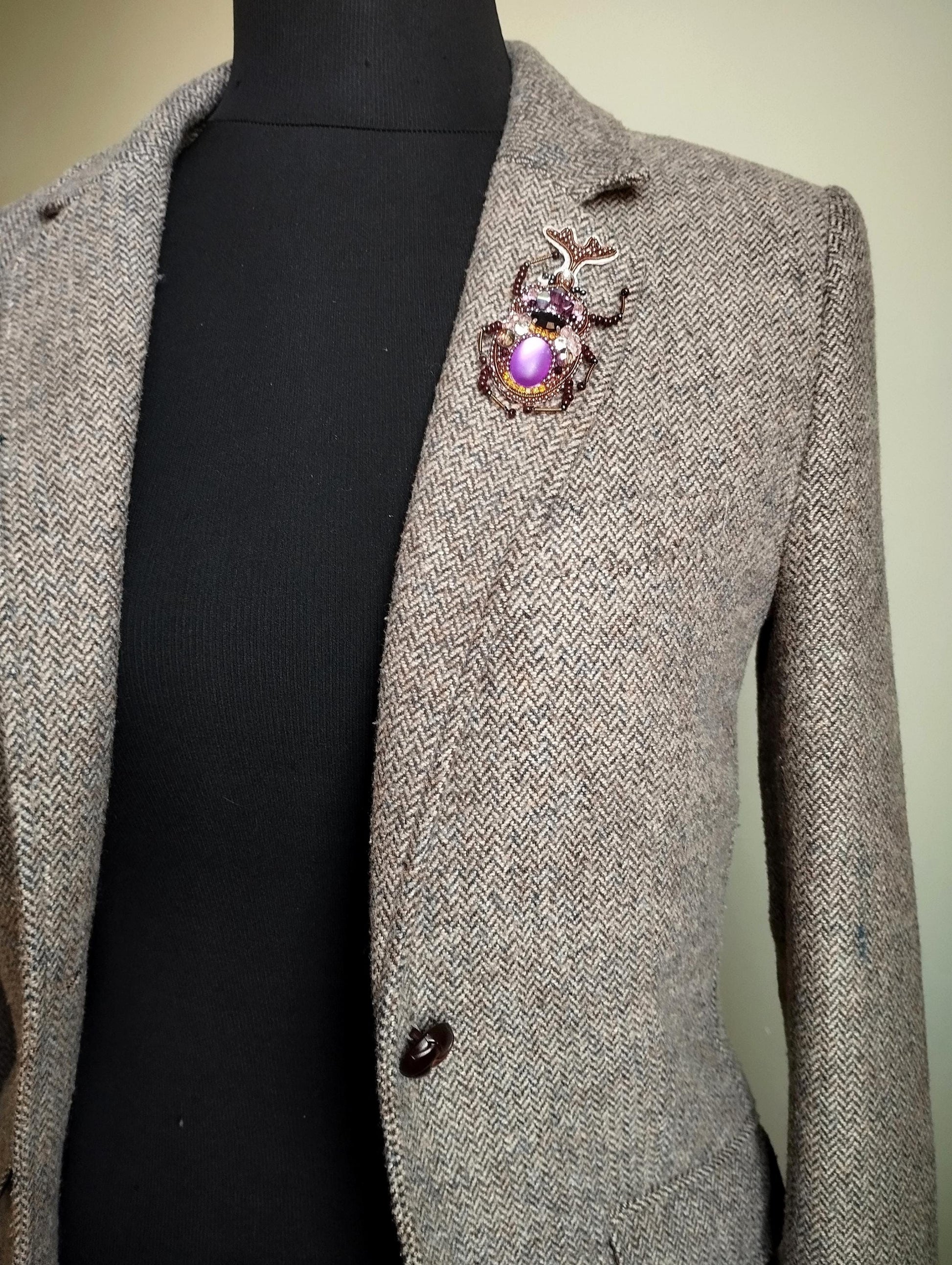 A gray tweed jacket with a purple and gold brooch on the left breast pocket area.