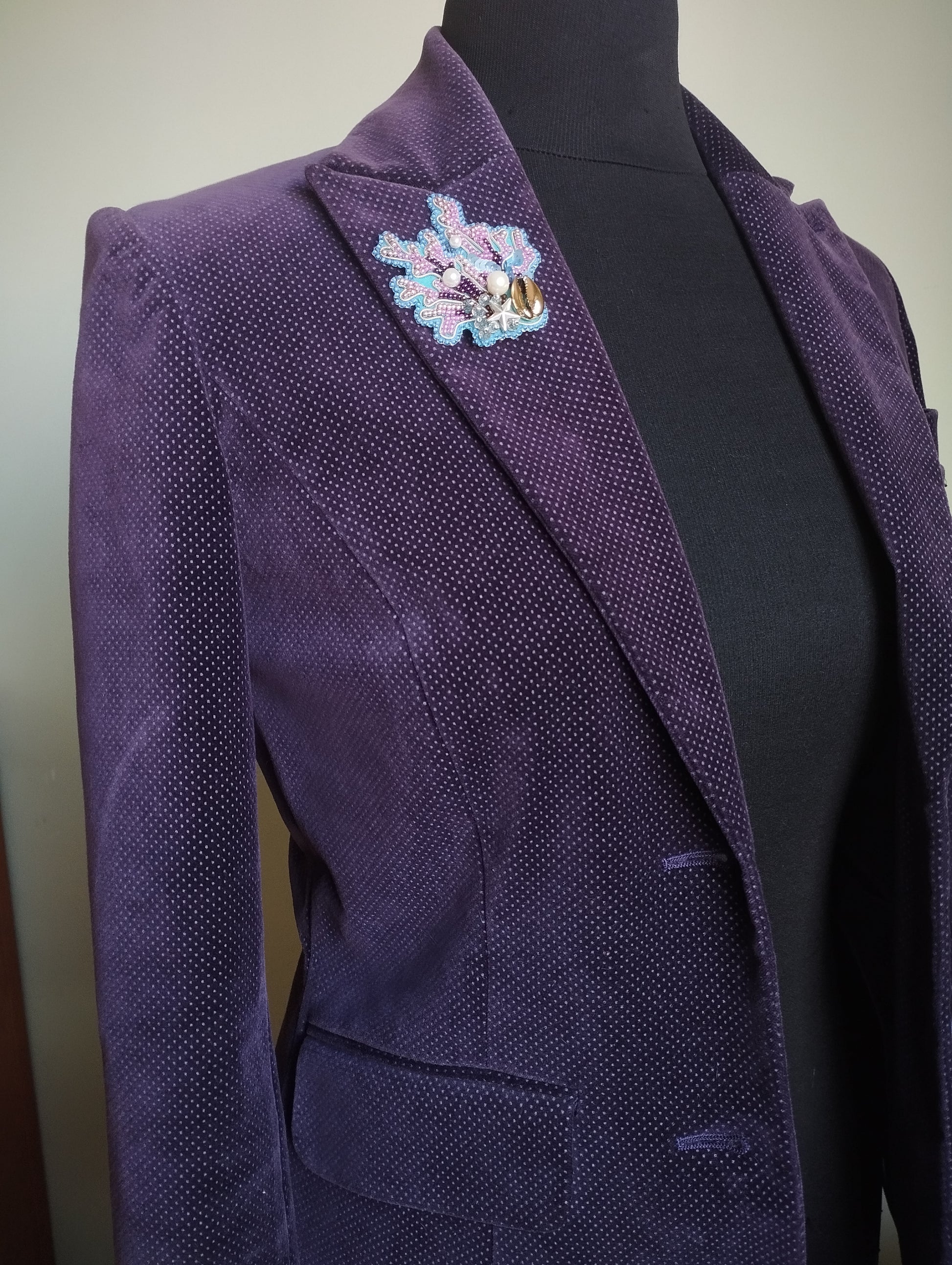 A purple velvet jacket with a floral brooch on the left side.