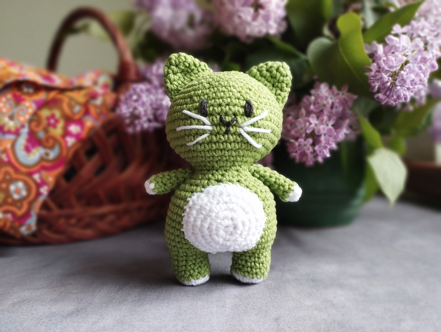a hand holding a small green crocheted cat