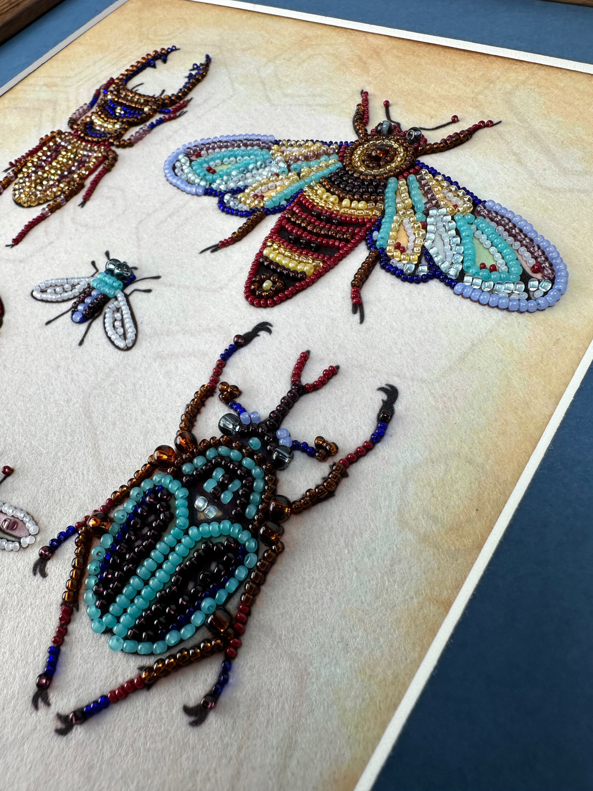 a close-up view of a detailed beaded artwork depicting various insects, including a large dragonfly and smaller insects.