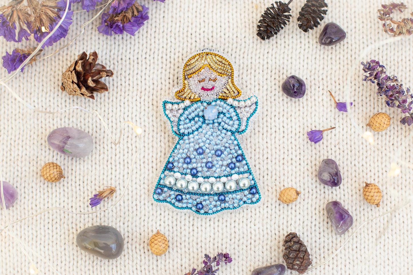 a decorative piece of a blue and white bead angel figure surrounded by various natural elements such as pine cones, gemstones, and dried flowers.