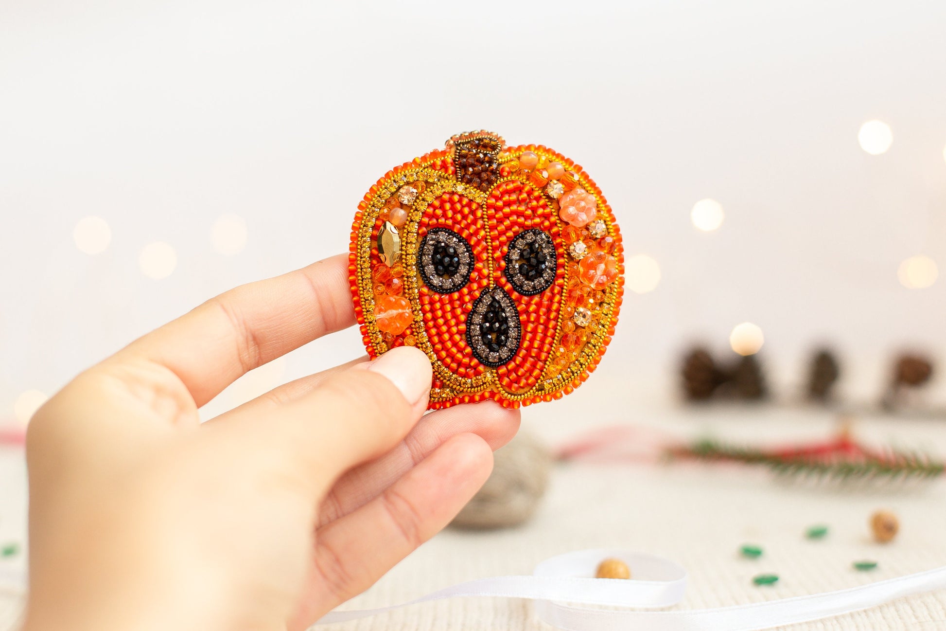 a hand holding a beaded pumpkin ornament