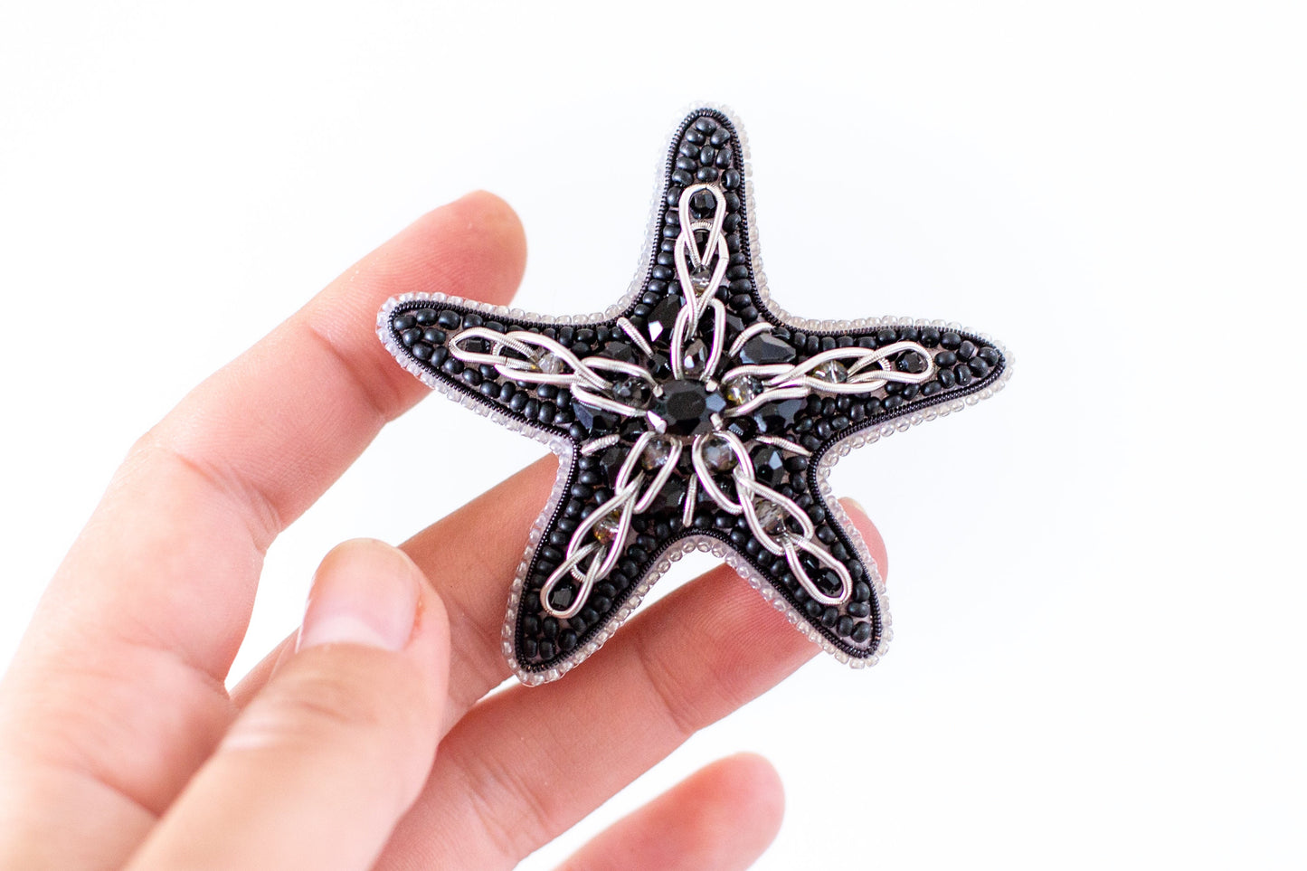 a hand holding a black and white starfish brooch