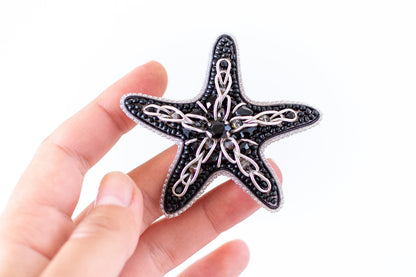 a hand holding a black and white starfish brooch