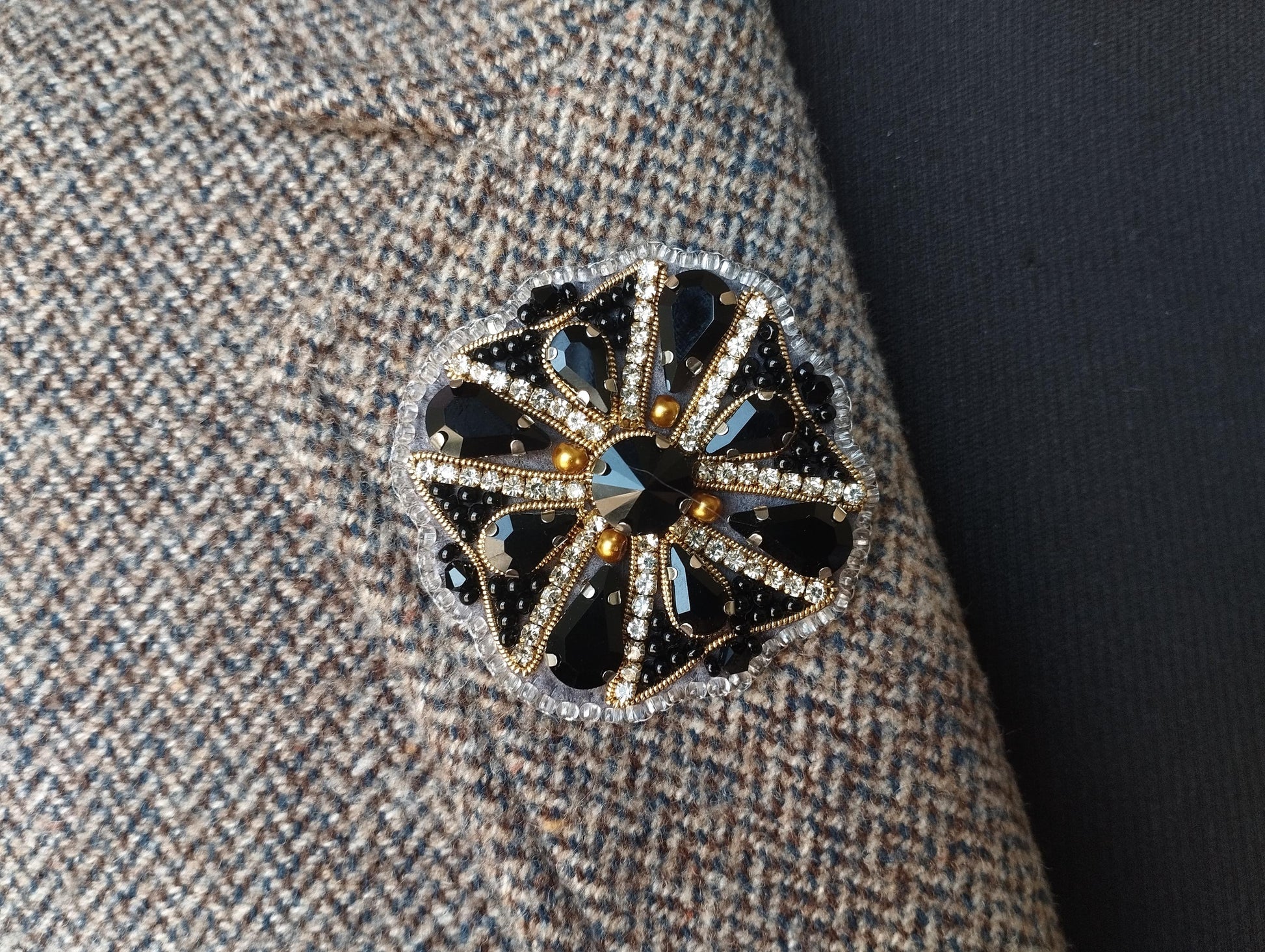 A close-up view of a decorative brooch or pin with a floral design and sparkling rhinestones or crystals attached to a fabric surface.