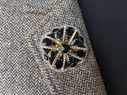 A close-up view of a decorative brooch or pin with a floral design and sparkling rhinestones or crystals attached to a fabric surface.