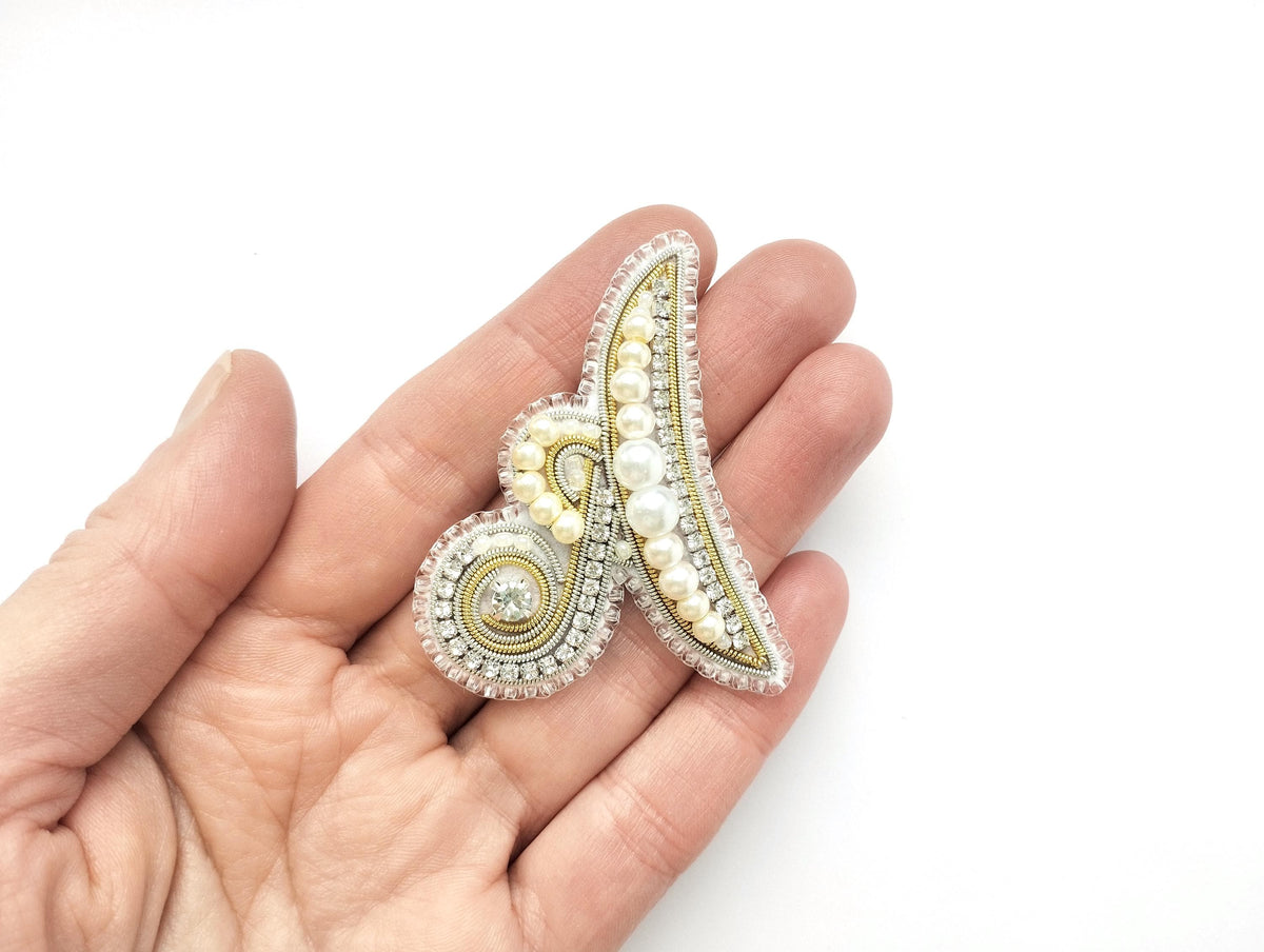 A hand holding a decorative piece of jewelry, which appears to be a beaded or embroidered item.