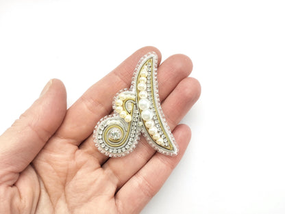 A hand holding a decorative piece of jewelry, which appears to be a beaded or embroidered item.